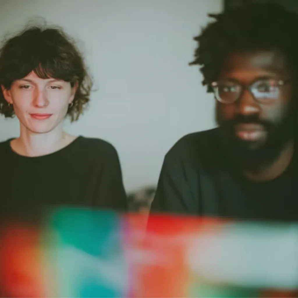 Two people look at a laptop screen, its colors glowing in the foreground.